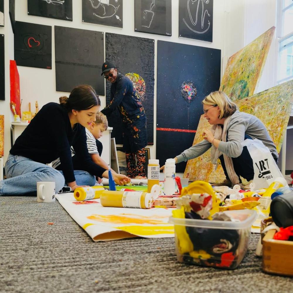 Children and adults painting together on a large canvas on the studio floor