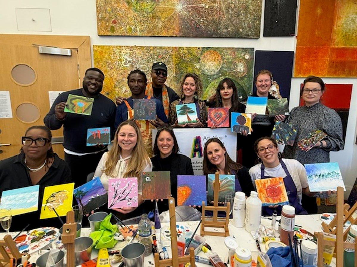 A group of workshop participants smiling and holding up their paintings in the Art-Alive studio