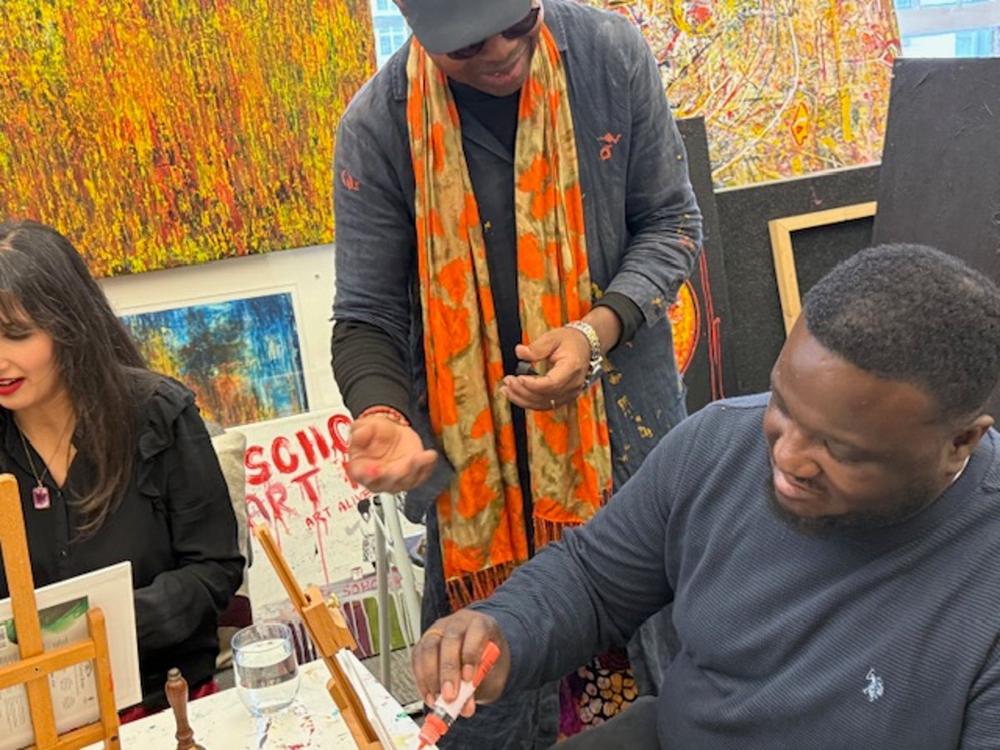 A tutor mentoring a young adult beside a table of paints and canvases