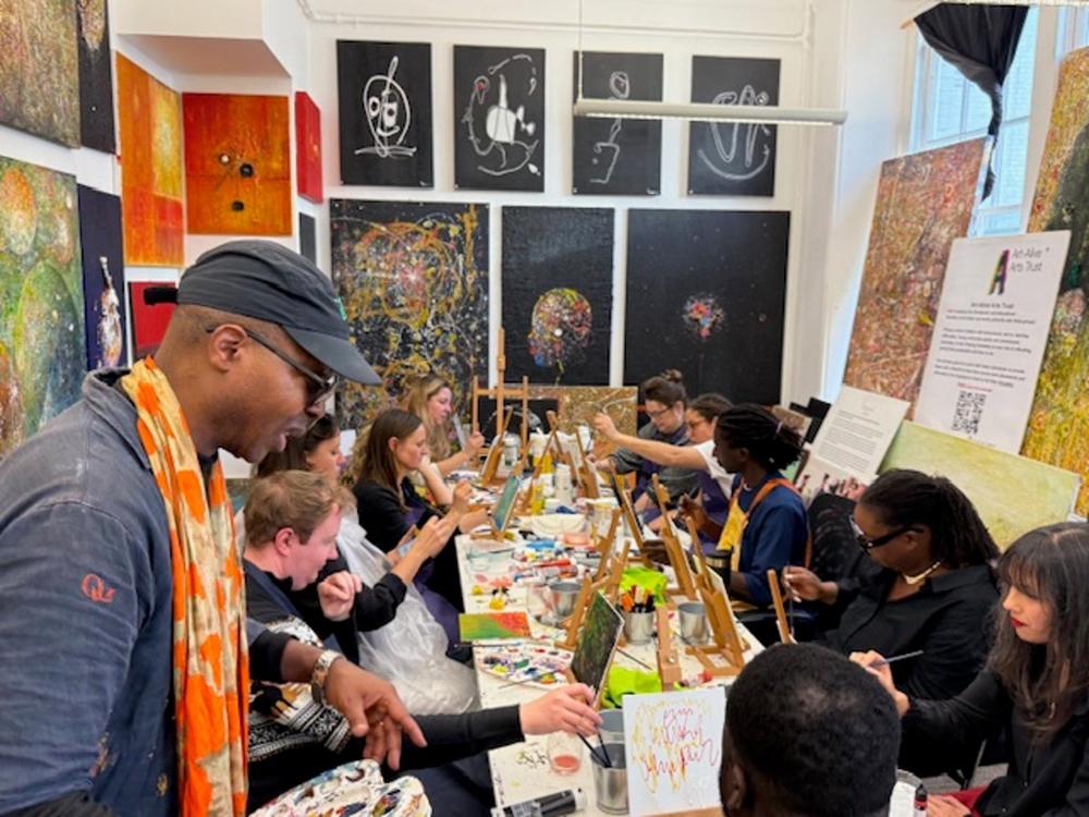 A long table of people painting in the Art-Alive studio, surrounded by artwork